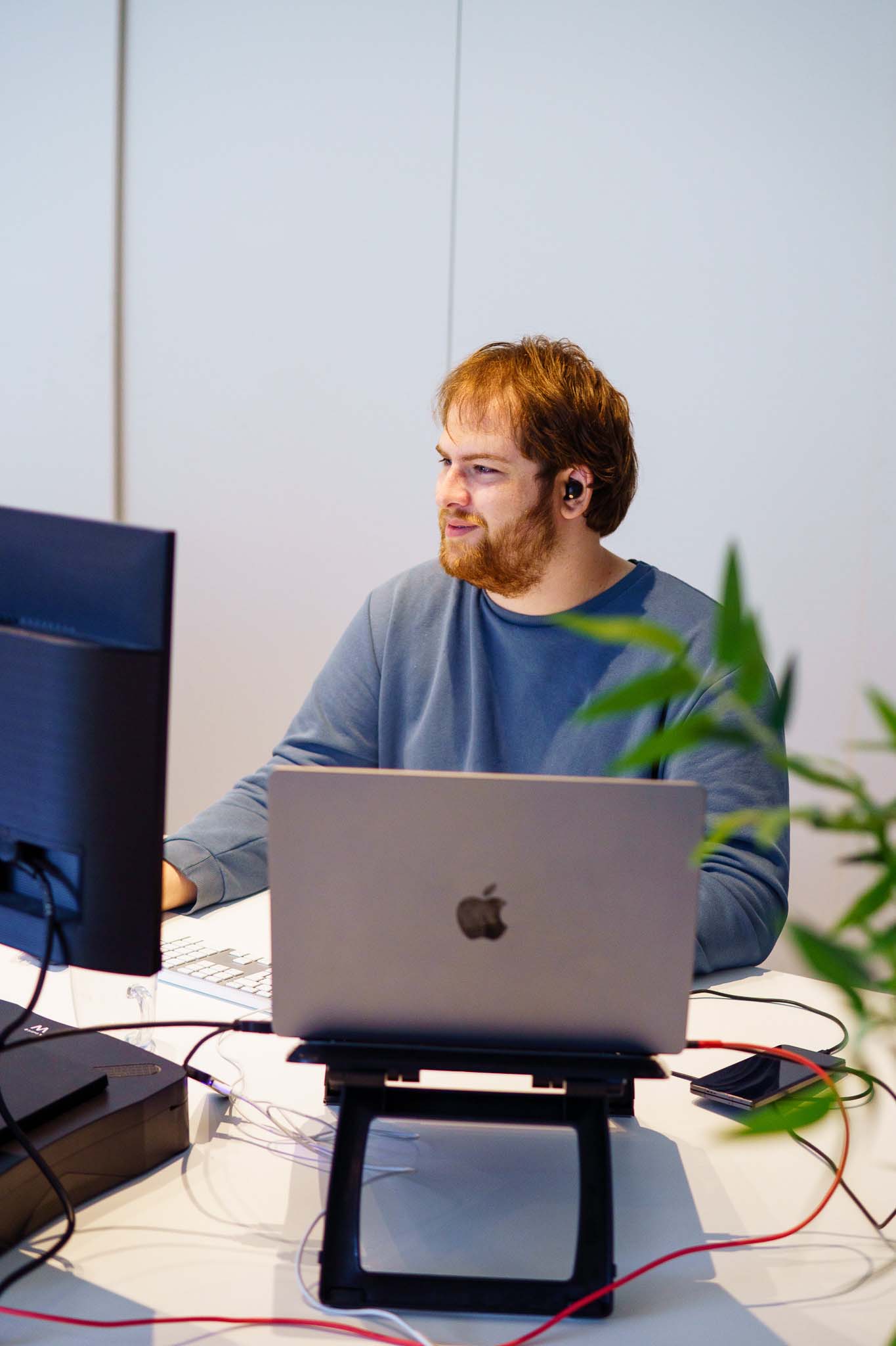 BURO210 Fullservice Marketingbureau Jonge man met rood haar werkt geconcentreerd achter zijn laptop en monitor op kantoor. Hij draagt oordopjes en heeft een rustige uitstraling.