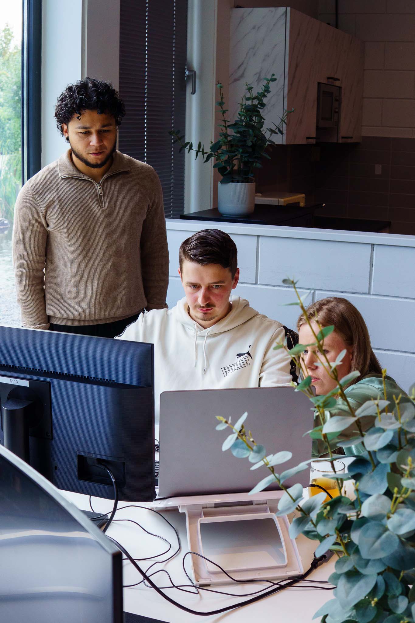 BURO210 Fullservice Marketingbureau Drie collega's werken samen aan een computer in een moderne kantooromgeving. Focus op teamwork en projectontwikkeling in een innovatieve setting.