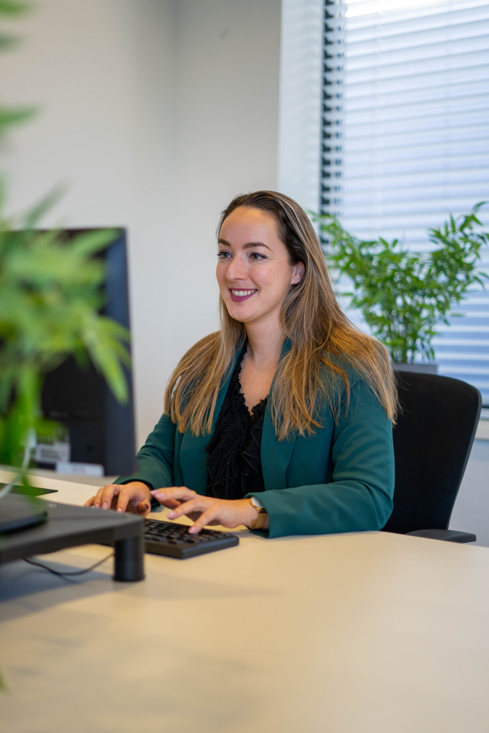 BURO210 Fullservice Marketingbureau Zakenvrouw in groene blazer werkt aan haar computer in kantoor. Het creëren van een sterke visuele identiteit voor professioneel gebruik.