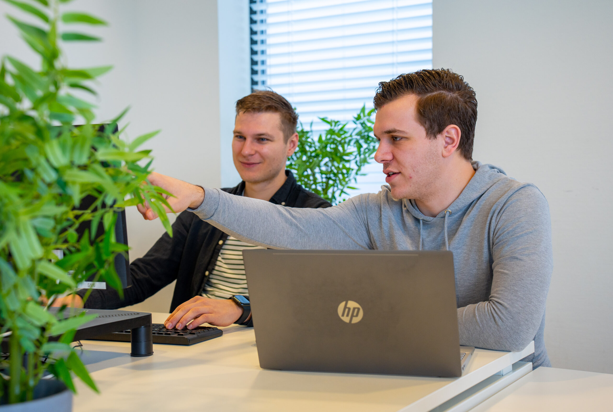 BURO210 Fullservice Marketingbureau Twee collega's werken samen aan de visuele identiteit van een project. Eén wijst naar het scherm, de ander typt op het toetsenbord met een laptop voor zich.